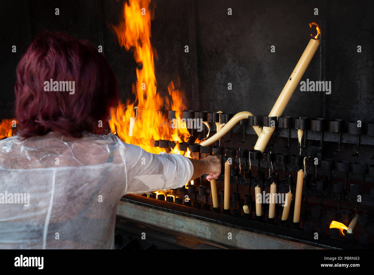 Una donna mette una candela votiva a bruciare nella pira come compimento della promessa fatta da Nostra Signora a Fatima in Portogallo Foto Stock