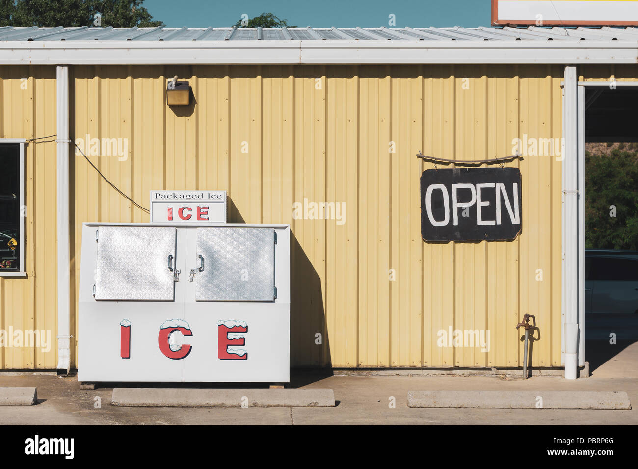 Confezionata alla macchina del ghiaccio contro una parete di colore giallo di un negozio di alimentari con un nero aperto cartello, Maupin, Oregon, Stati Uniti d'America. Look vintage. Foto Stock