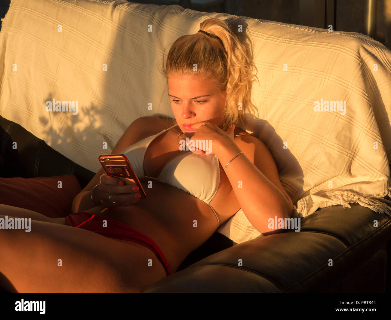 Una bella ragazza bionda controllando il suo telefono in un bikini all'interno di una casa Foto Stock
