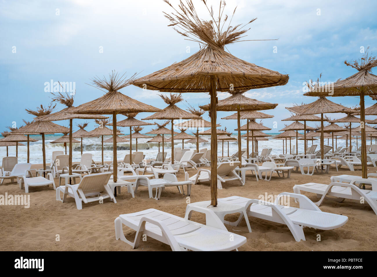 Vimini ombrelloni con chaise-longue sulla spiaggia Foto Stock