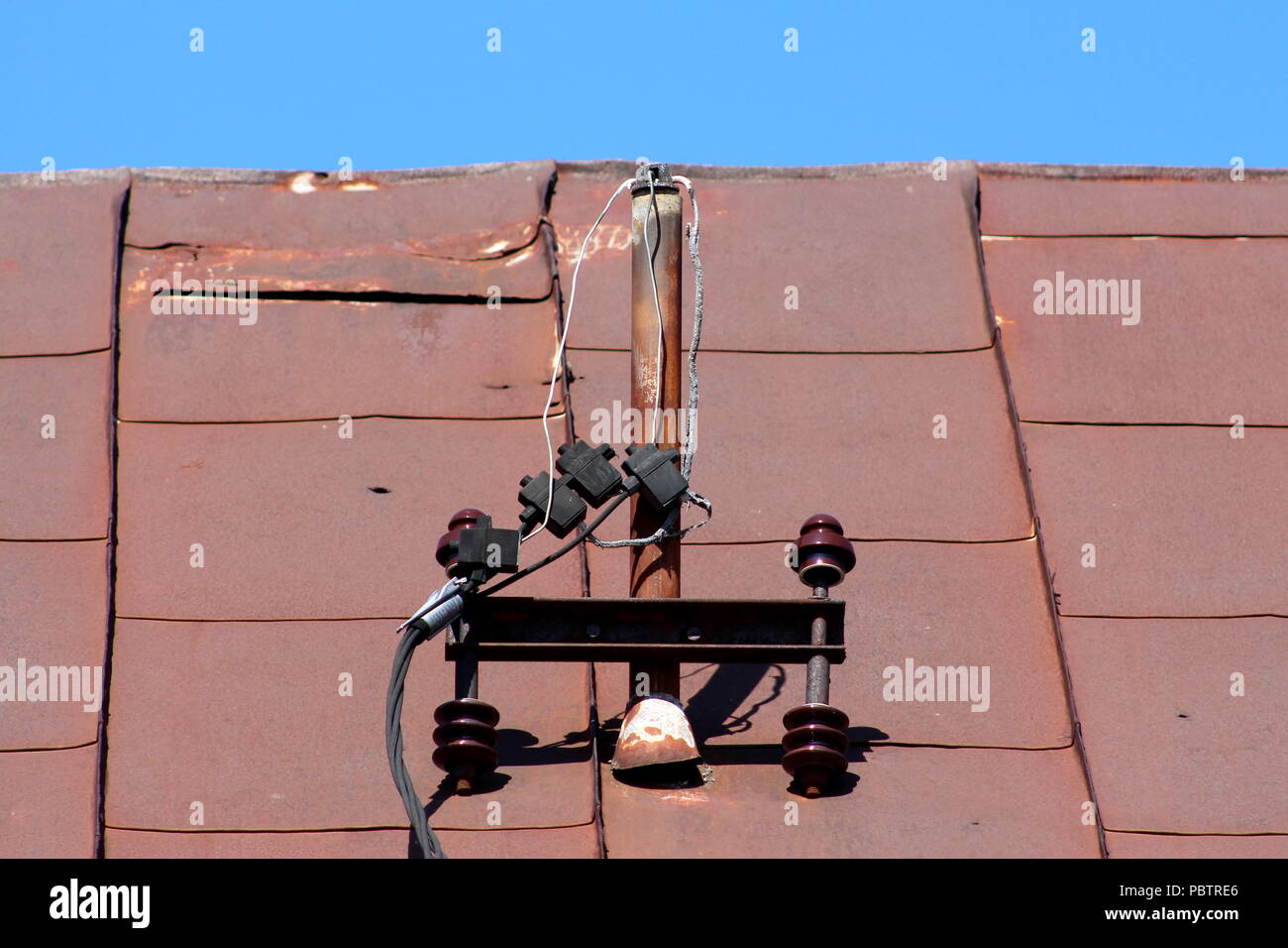 Metallo arrugginito pole con rotture di isolatori ceramici e tagliare verso il basso elettrico fili powerline appesi da metallo arrugginito tegole del tetto sul cielo blu chiaro backgr Foto Stock