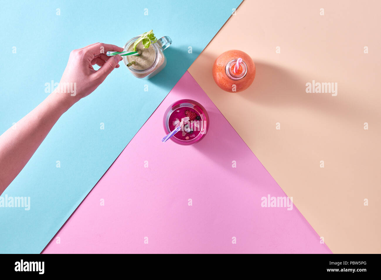 Tre frullati colorati servita in un vaso e una donna di mettere mano una cannuccia su carta colorata sullo sfondo Foto Stock