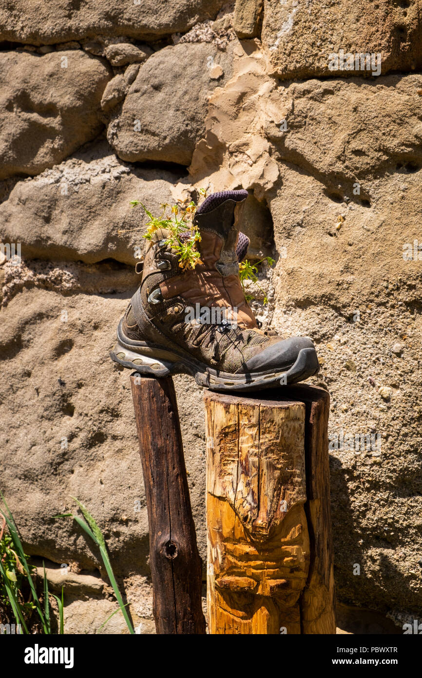 Ben indossati vecchio boot a piedi su un post da un muro di pietra con erbacce che crescono in Garrotxa zona vulcanica, Catalogna, Spagna Foto Stock