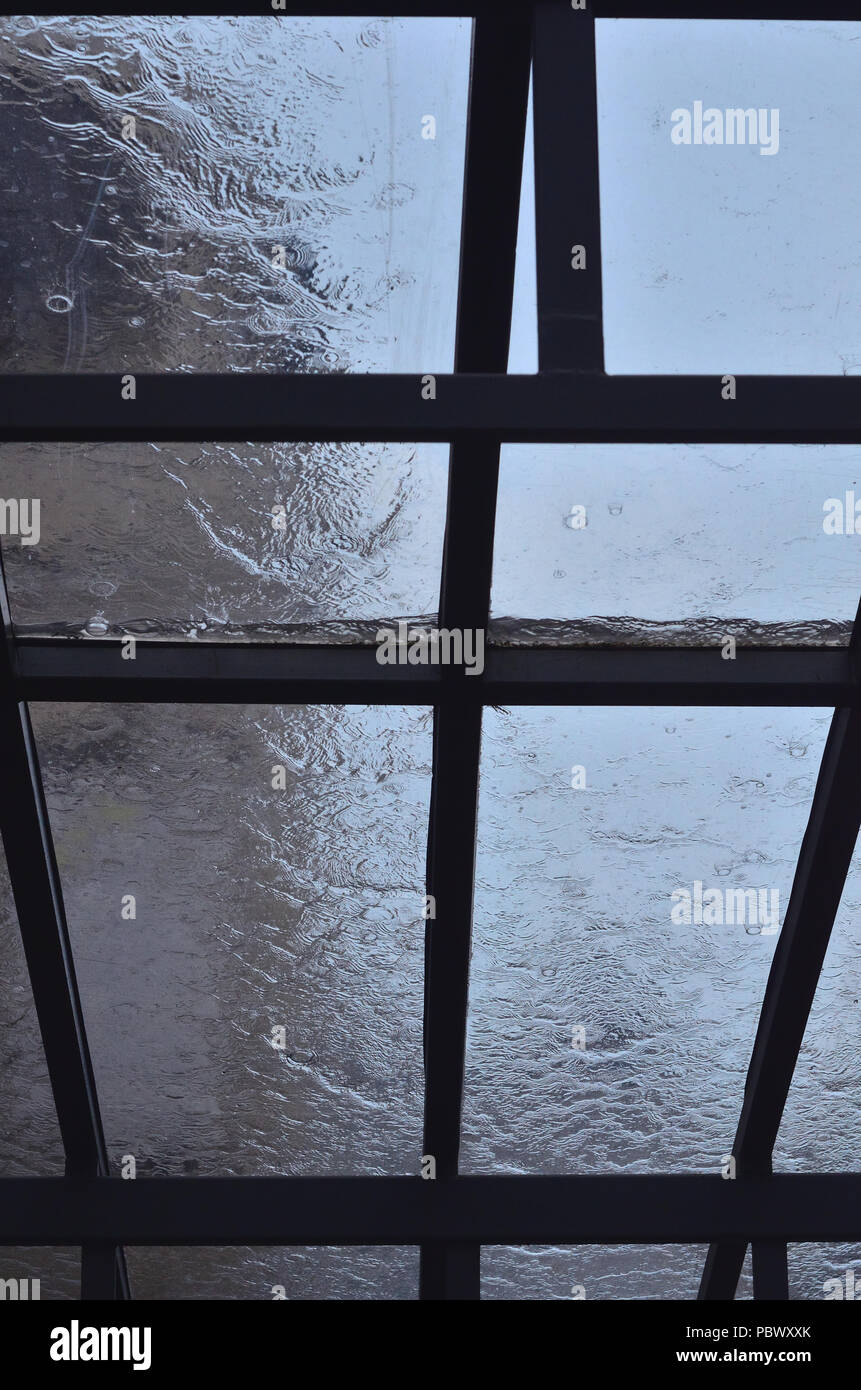 Una pesante pioggia si riversa su una finestra con cornici di legno, il cielo è visibile al di fuori della finestra Foto Stock