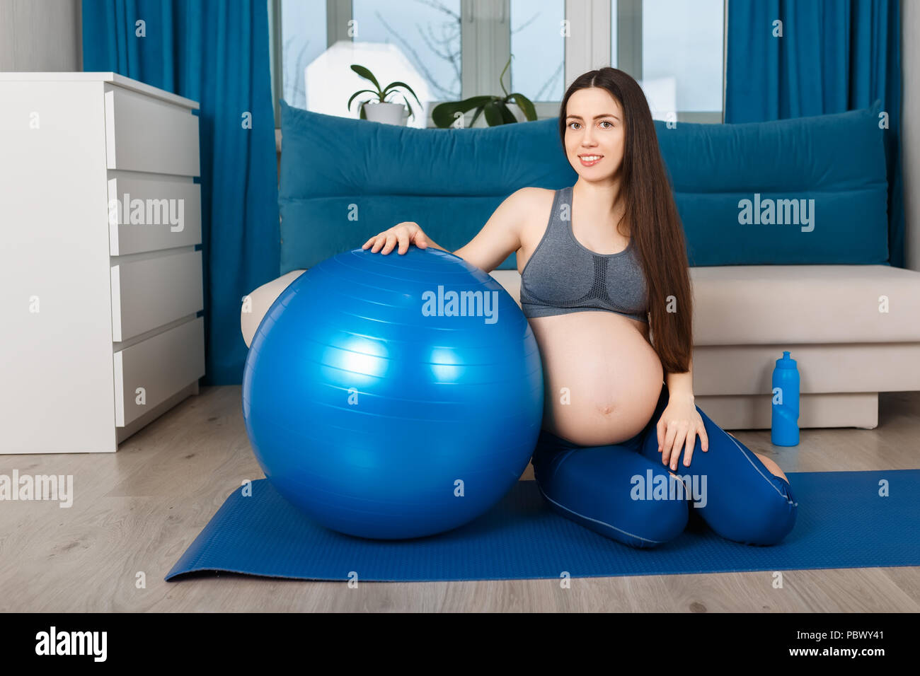 Felice donna incinta con blue montare la sfera seduto sul materassino yoga. Madre in attesa dopo la ginnastica a casa Foto Stock