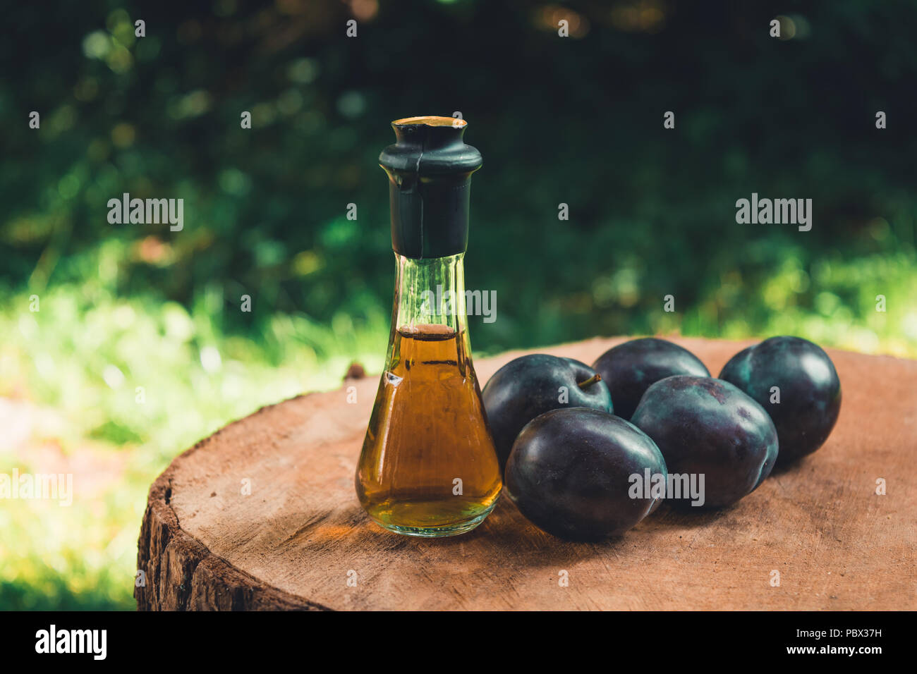 Acquavite di prugne (Slivovitz) in serbo tradizionale bottiglia di vetro con fresche susine mature su una superficie di legno. Foto Stock