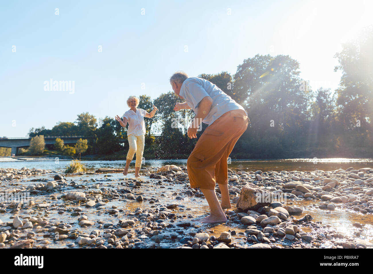 Divertente coppia senior giocando con acqua al fiume in una giornata di sole Foto Stock