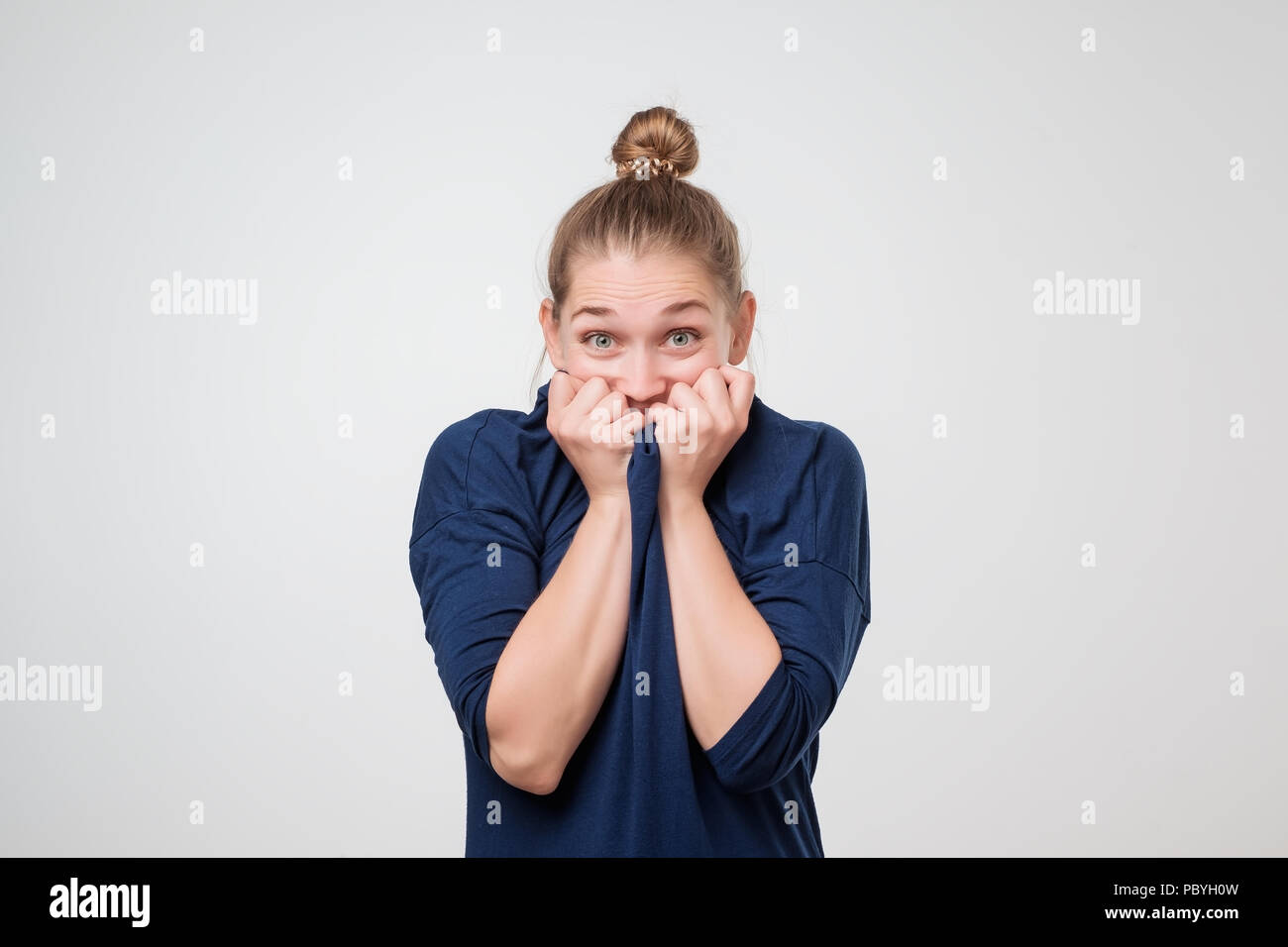 Giocoso timida donna europea in maglietta blu nasconde il viso con le mani Foto Stock