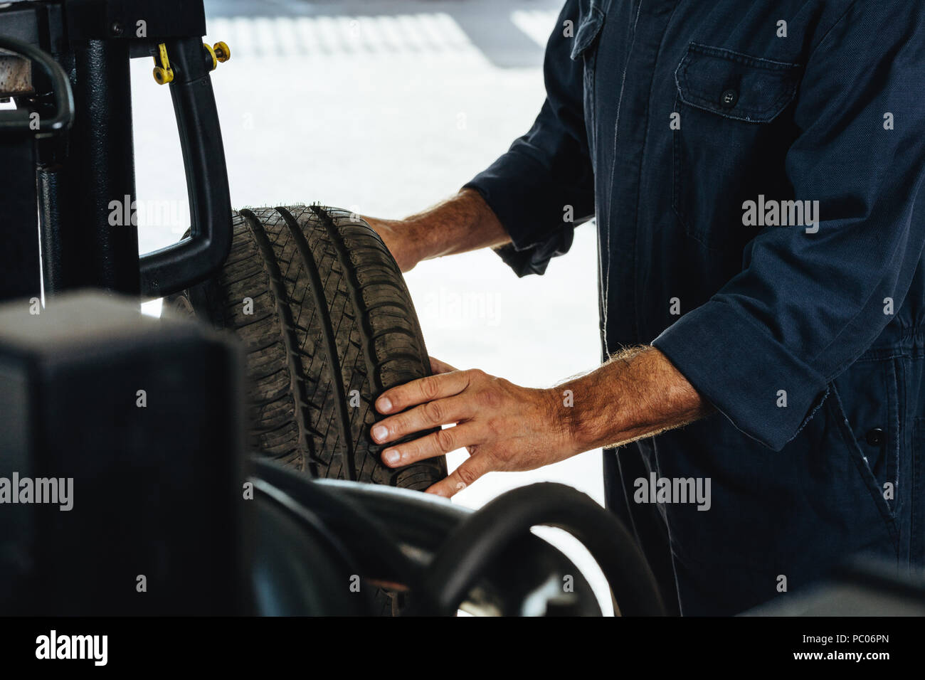 Tagliate il colpo di un meccanico di controllo della condizione di una ruota di automobile. Uomo di esaminare il grado di usura dei pneumatici per auto in garage. Foto Stock