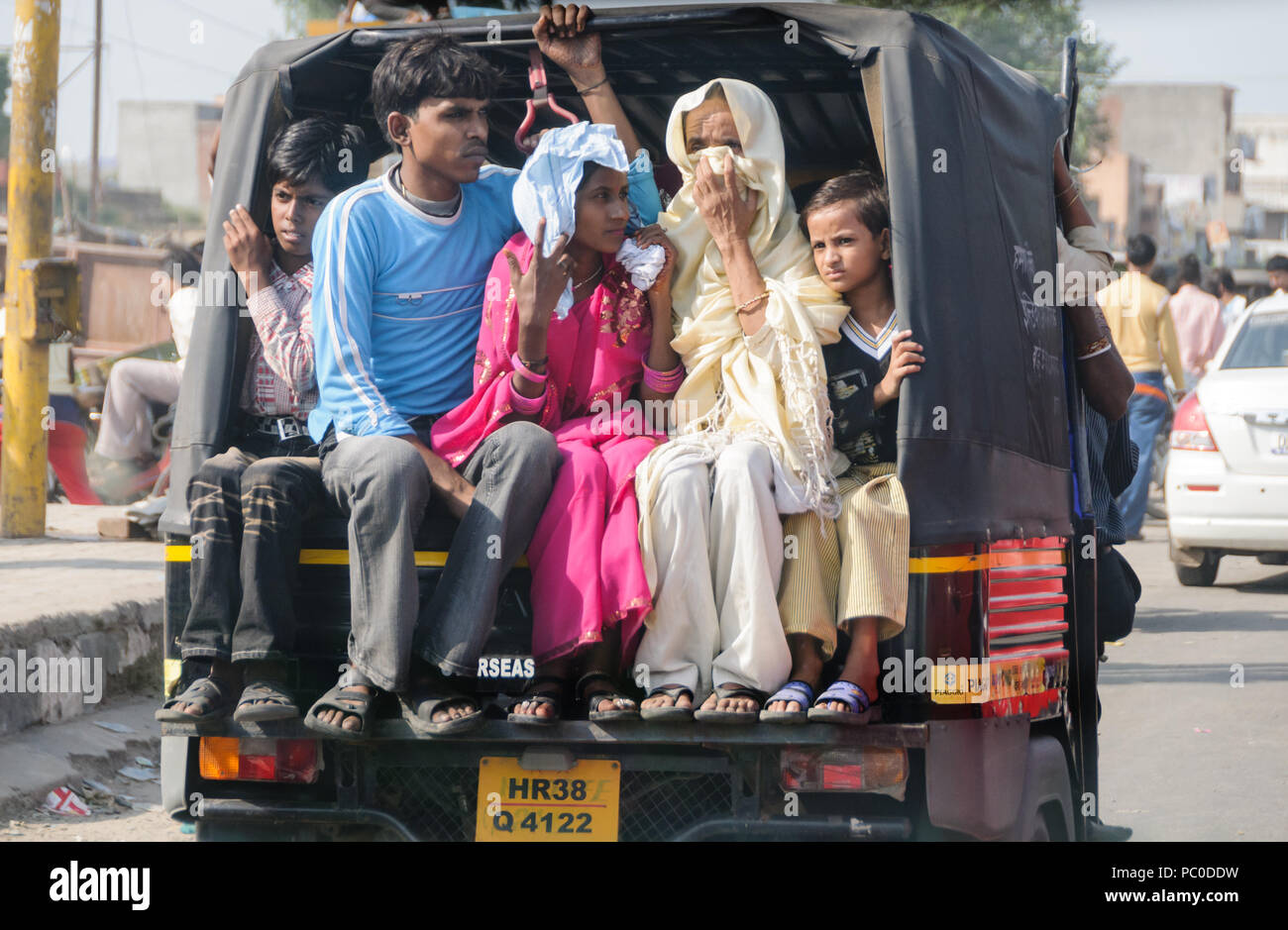 Famiglia di cinque persone stipate in aperto sul retro di un veicolo in Mumbai, India, con la madre che copre la bocca per evitare di inalare fumi di scarico Foto Stock