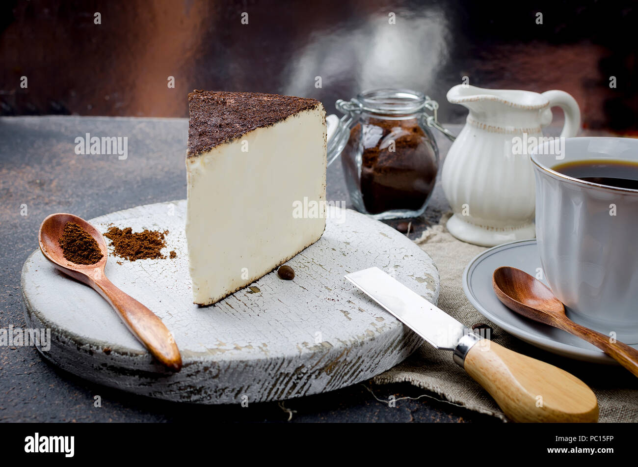 White tazza di caffè nero con un pezzo di formaggio morbido in un caffè o la cheesecake su sfondo scuro, spazio di copia Foto Stock