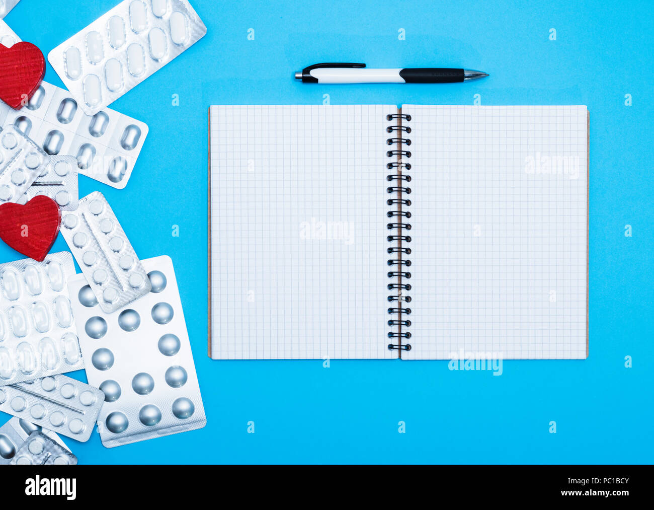 Aprire il notebook nella cella vuota con fogli bianchi e una penna, lato della confezione con compresse bianche, vista dall'alto Foto Stock