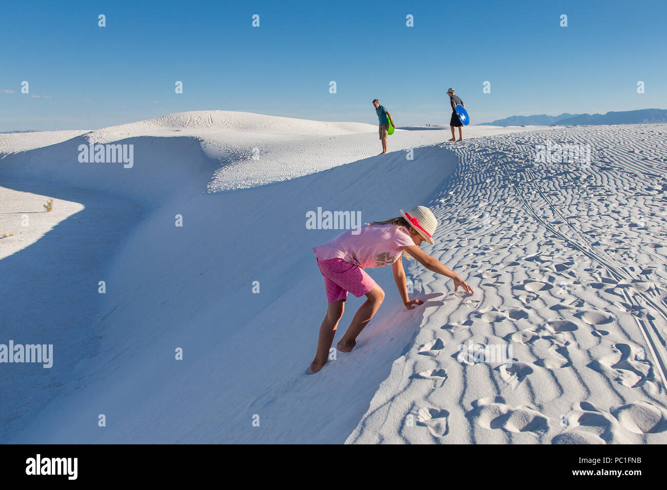 Una ragazza si arrampica un bianco dune di sabbia con la sua famiglia in background. Foto Stock
