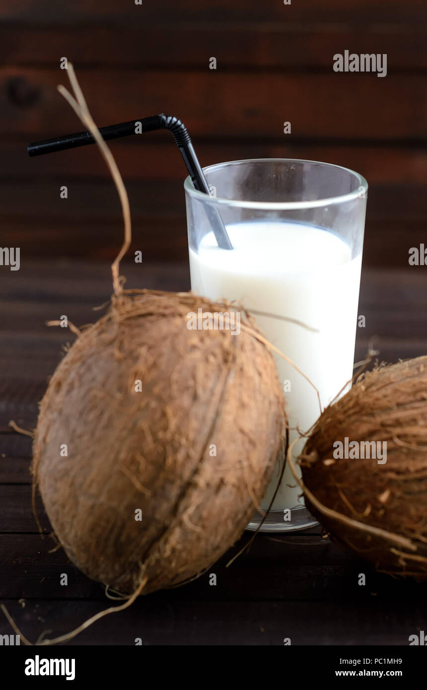 Un bicchiere di latte di cocco e due noci di cocco intero su sfondo di legno. Foto Stock