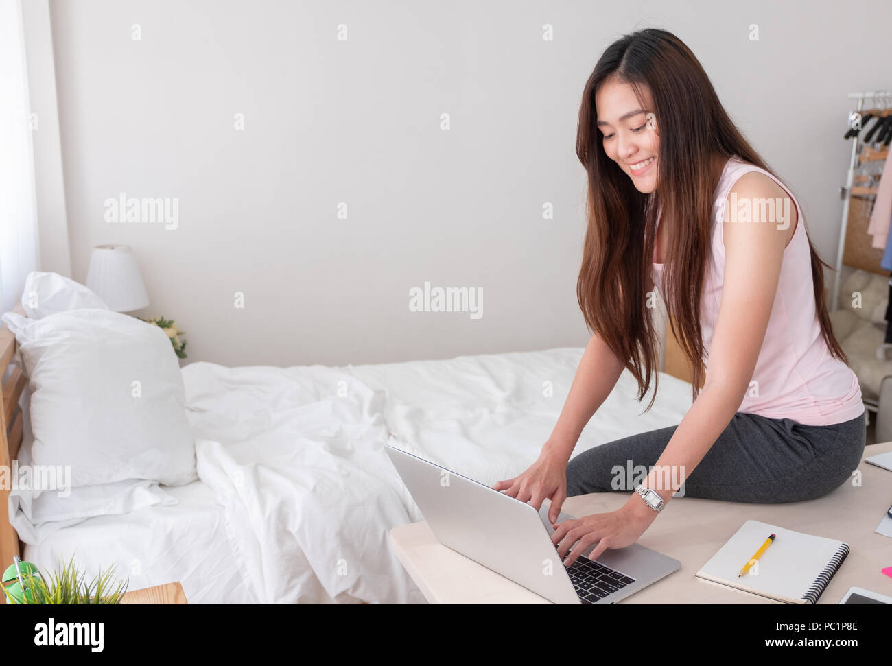 Femmina asiatica del freelancer giubbotto di usura shirt digitazione sul computer portatile sul tavolo e pensare al lavoro nella camera da letto di casa.Il lavoro a casa.facendo scartoffie da casa Foto Stock
