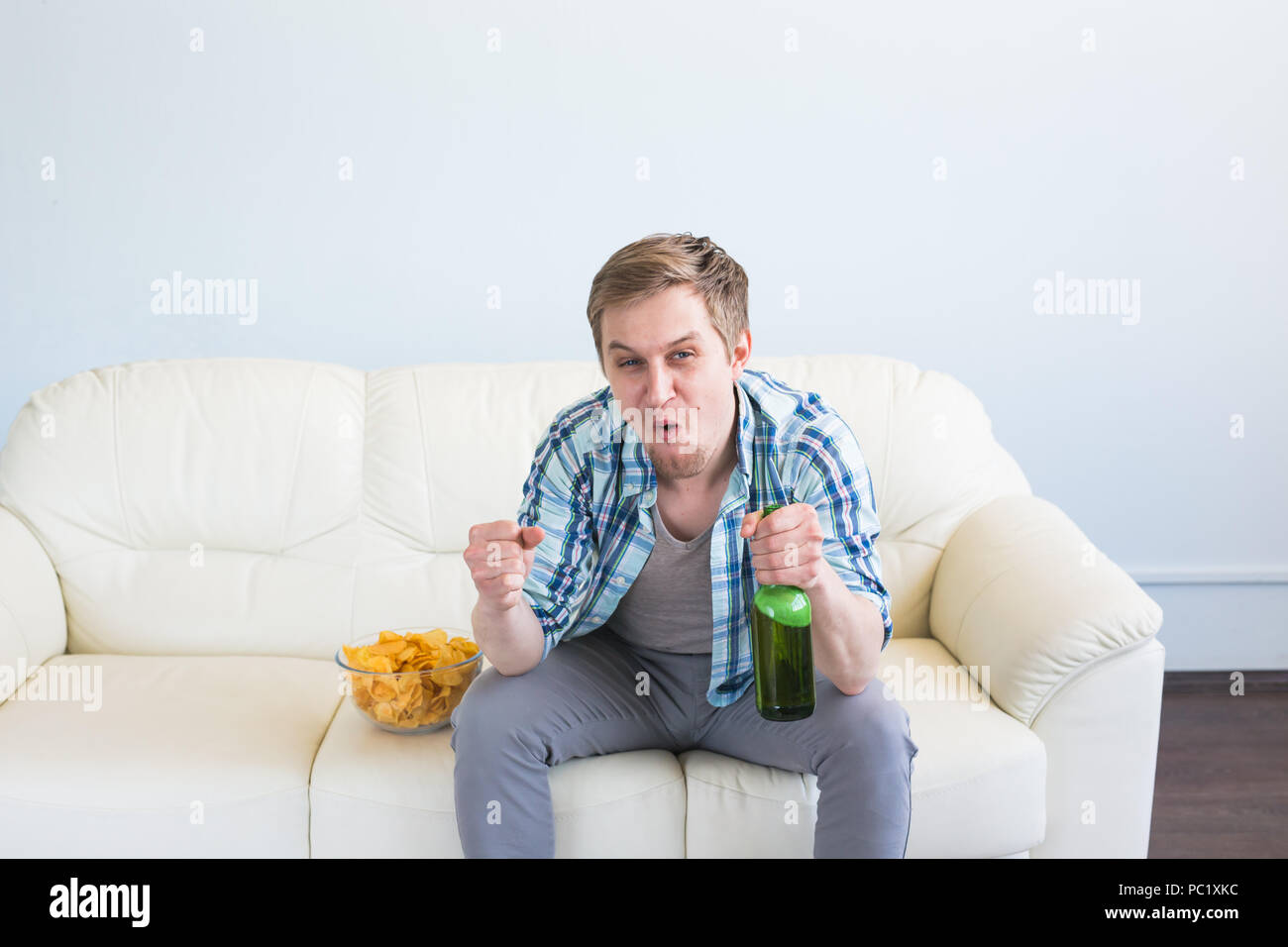 Uomo con birra e patatine guardando la TV a casa Foto Stock