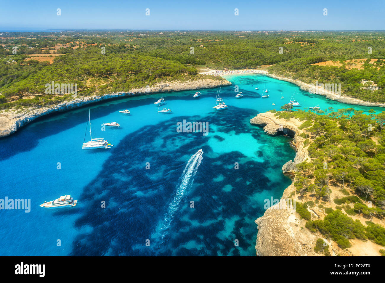 Vista aerea del mare trasparente con acqua blu, spiaggia sabbiosa, rocce, alberi verdi, yacht e barche nella mattina di sole in estate. Viaggiare a Maiorca, Bale Foto Stock
