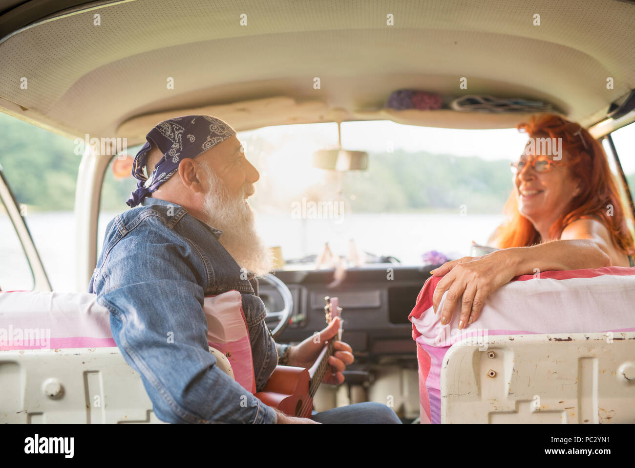 Un vecchio hipster giovane seduto in un furgone, l'uomo la riproduzione di ukulele Foto Stock