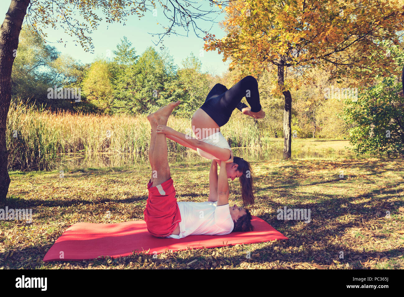 Giovane facendo acro yoga nel parco dell'autunno. Ottobre. Donna incinta. Messa a fuoco selettiva Foto Stock
