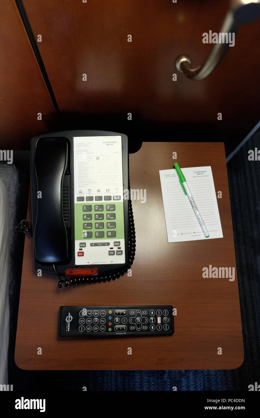 Comodino a un Courtyard Marriott hotel con telefono, telecomando per la televisione e la penna e il taccuino di scrittura. Foto Stock