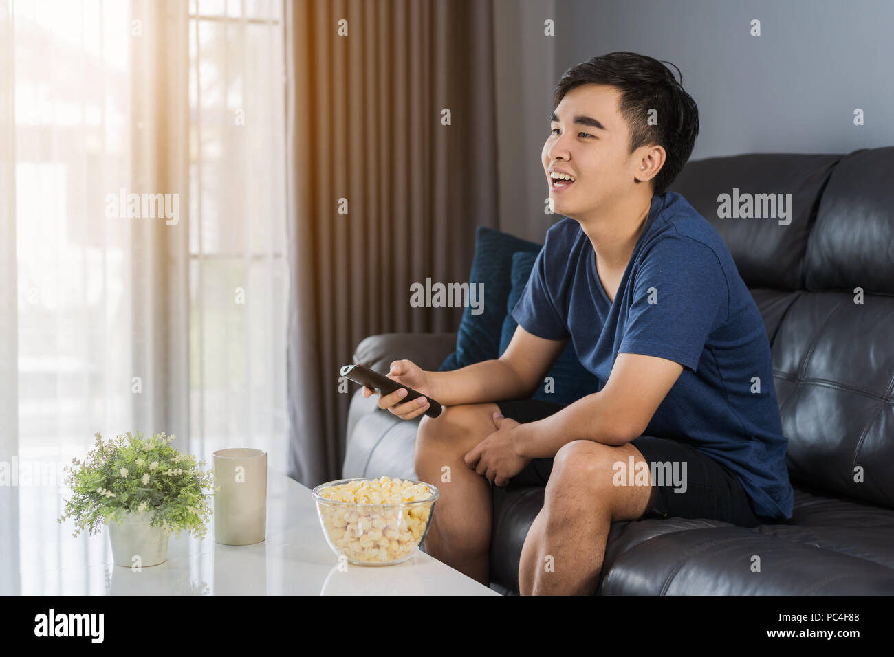 Allegro giovane uomo con telecomando e guardando la TV comodamente seduti sul divano del soggiorno Foto Stock