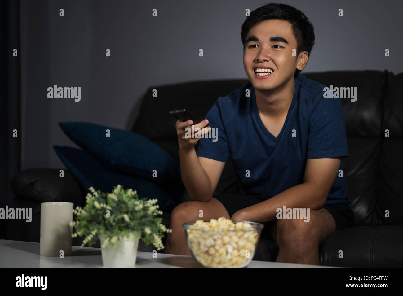 Allegro giovane uomo con telecomando e guardando la TV comodamente seduti sul divano di notte Foto Stock