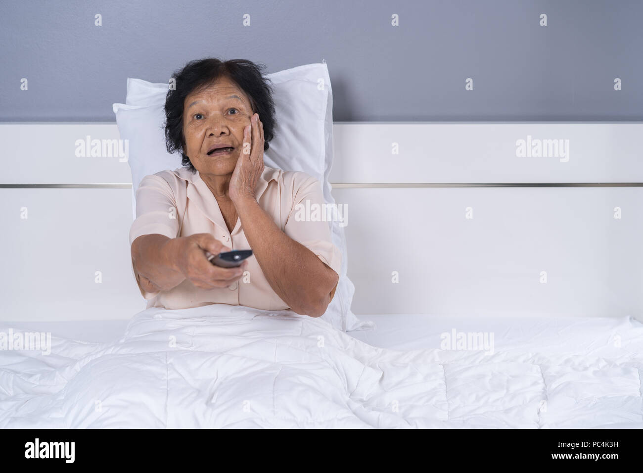 Senior donna guarda la paura filmato con il telecomando del televisore su un letto Foto Stock