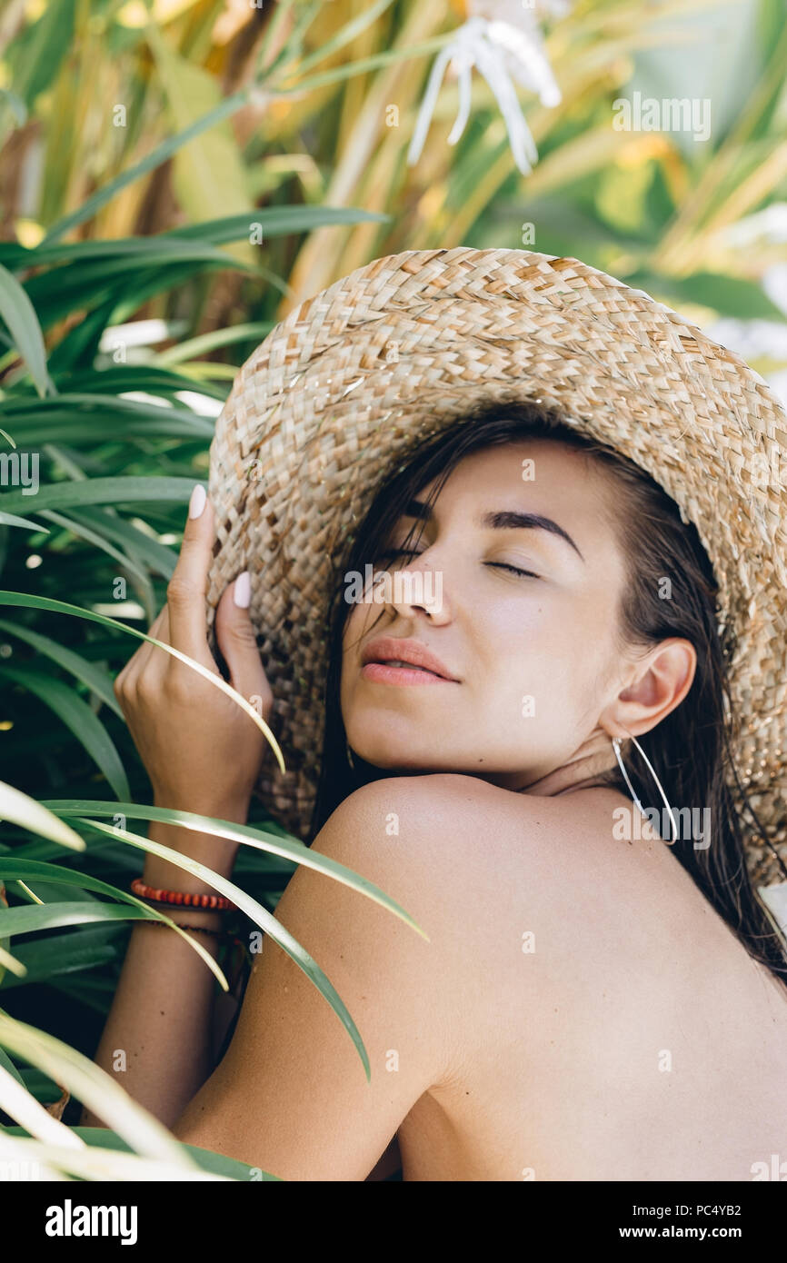 Colorata estate Ritratto di giovane attraente brunette donna che indossa gli occhiali da sole sotto una palma dalla piscina, Foto Stock