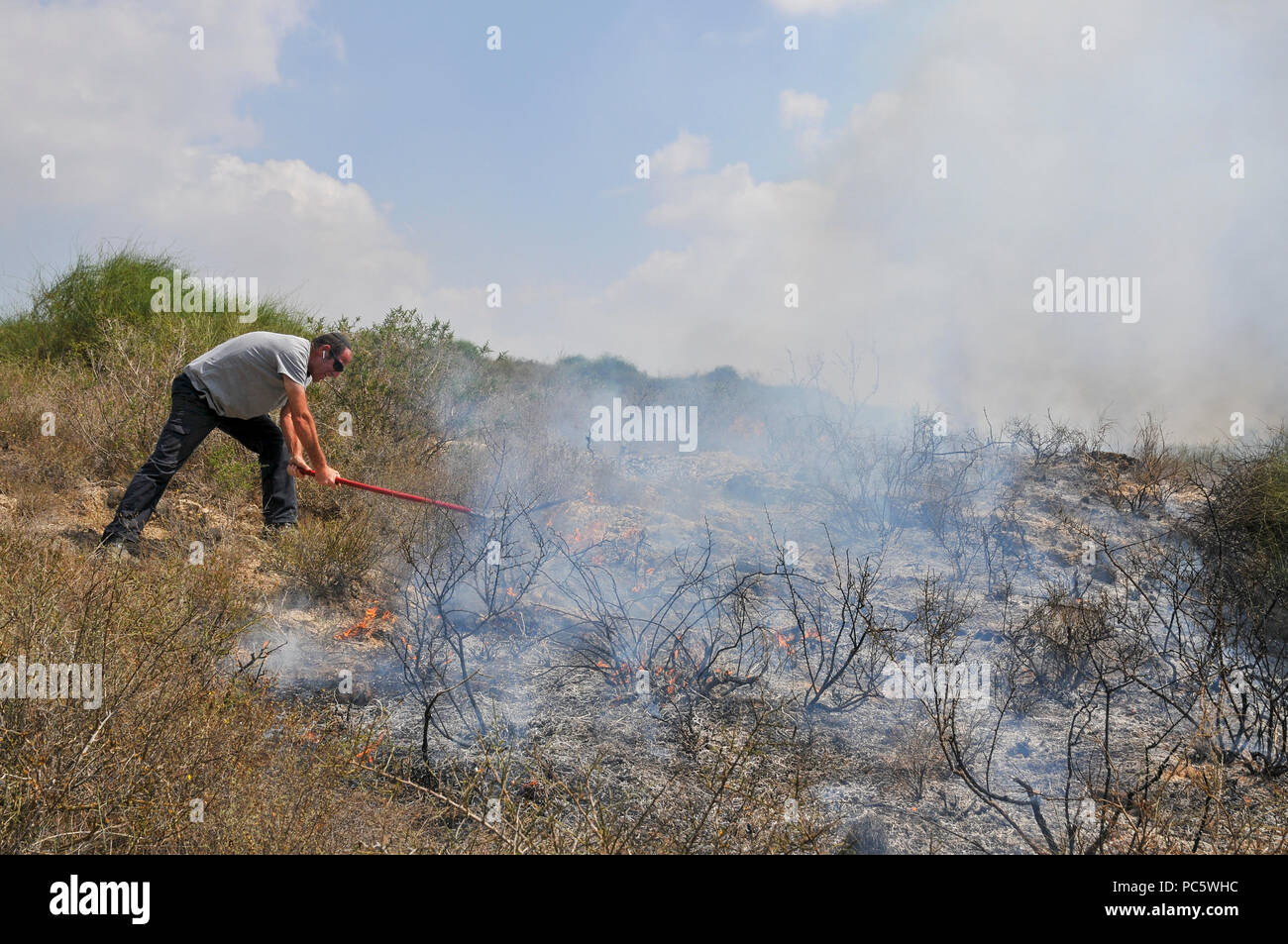 L'uomo cerca di estinguere ancora un altro incendio causato da Kite palestinese bombe che sono state percorse da Gaza con un acceso benzina panno imbevuto per impostare gli incendi per Foto Stock