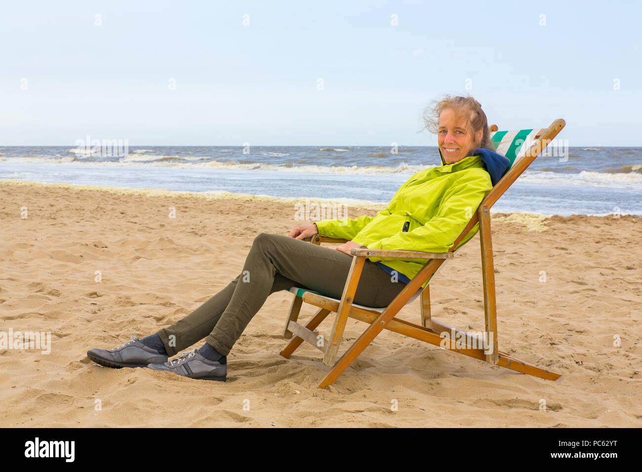 La donna caucasica con giacca estiva seduto nella sedia spiaggia in riva al mare Foto Stock