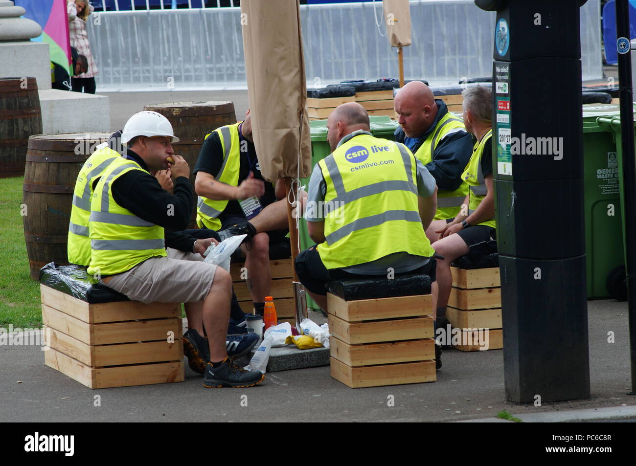 I lavoratori che indossa il verde ad alta visibilità gilet stanno prendendo una pausa pranzo seduti su cassette di legno. Foto Stock