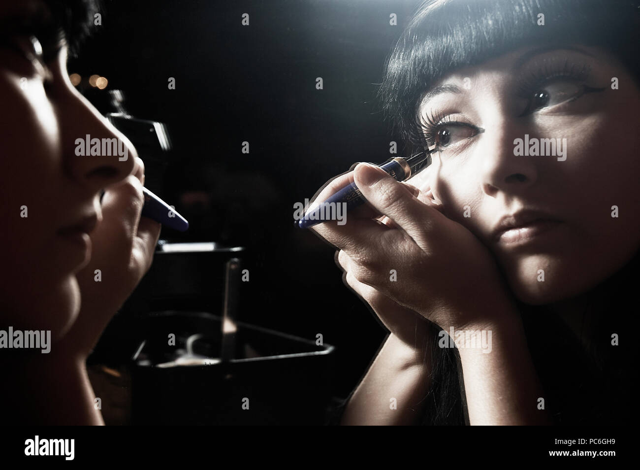 Una donna di goth si applica il suo make-up nello specchio. Foto Stock