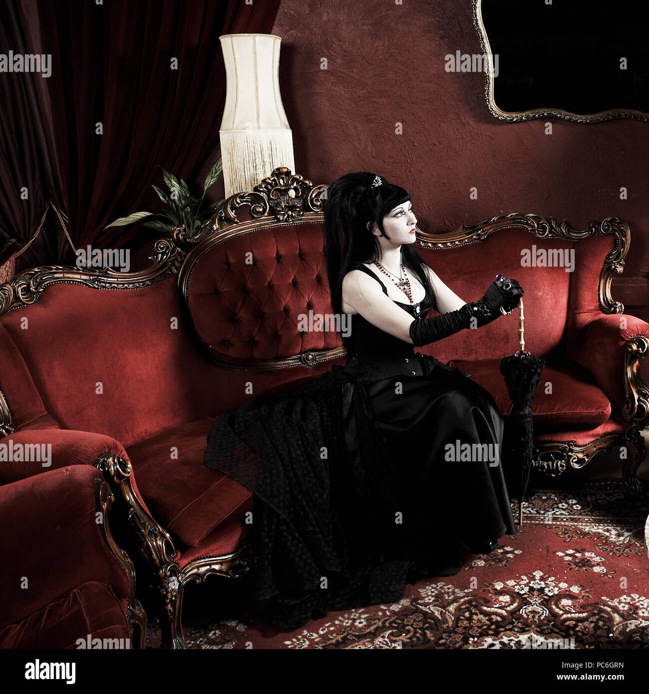 Un palazzo gotico donna seduta in un salotto indossando un corsetto e tenendo un ombrellone. Foto Stock