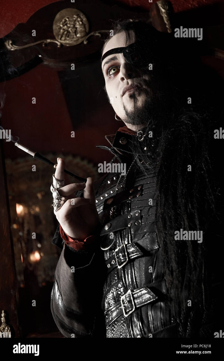 Un uomo gotico indossando un pirata eye-patch e fumare una sigaretta usando un bocchino. Foto Stock
