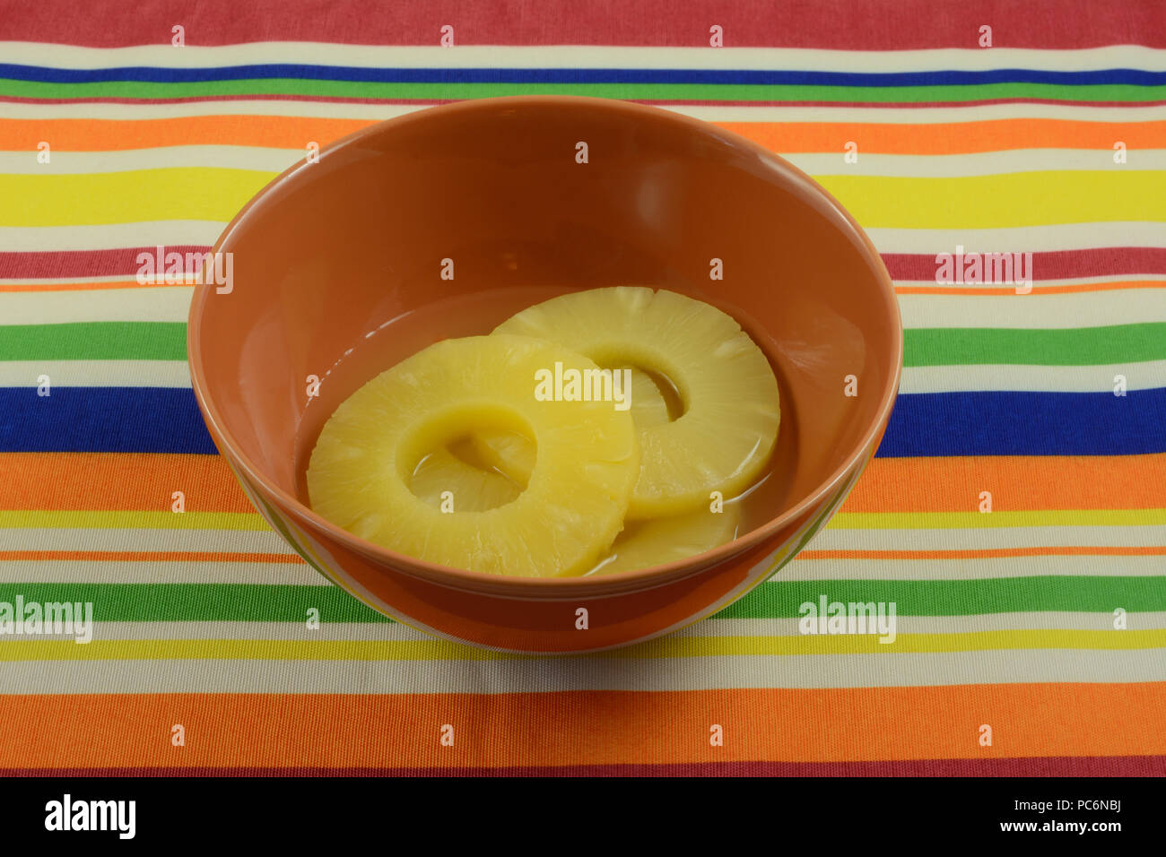 Conserve di anelli di ananas in succo di ananas in Orange Bowl sul posto a strisce mat Foto Stock
