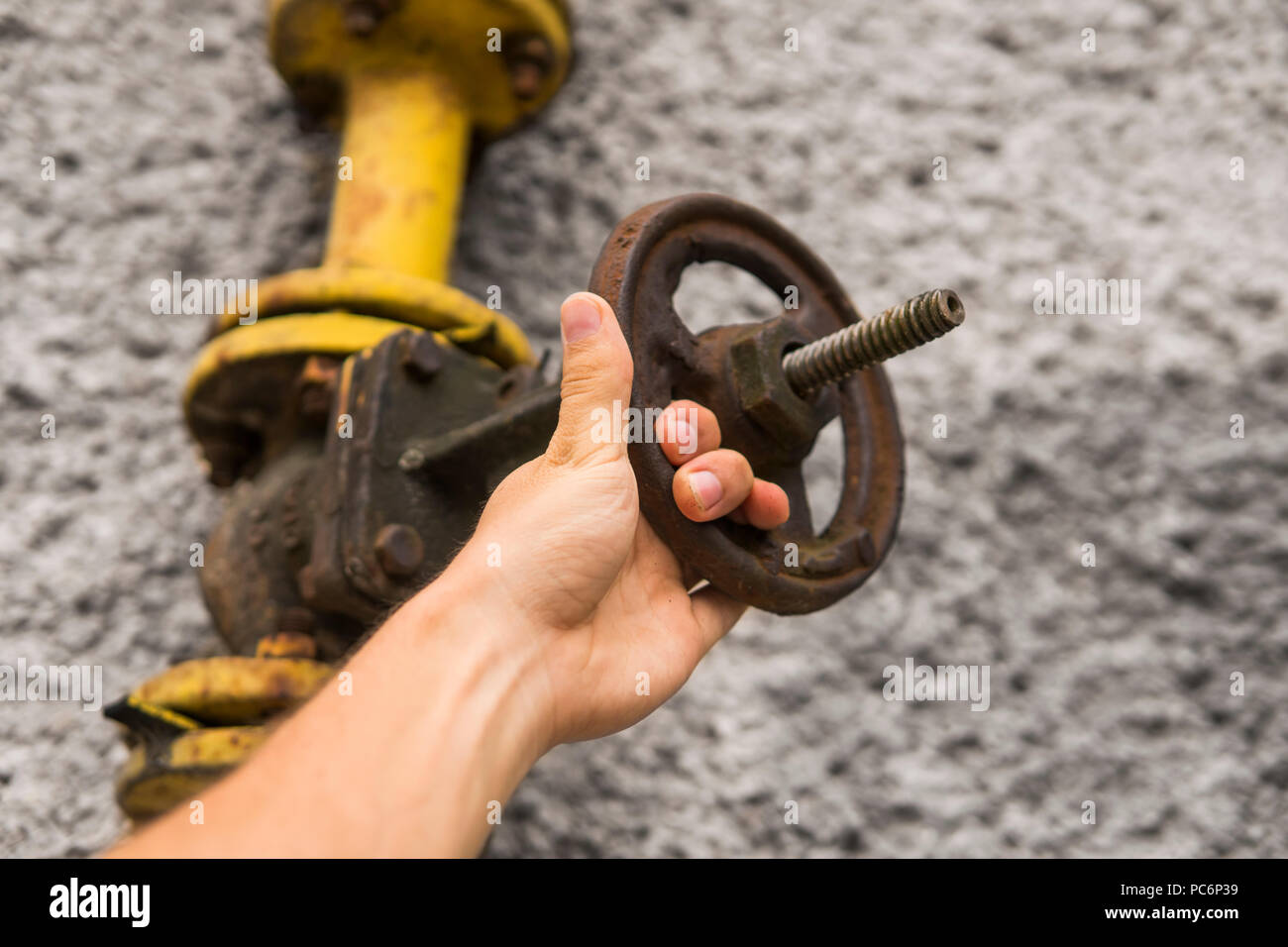 L uomo vecchio di contenimento di gas a spiovente gru sullo sfondo di un muro grigio. Antico cancello di gas di colore giallo è su un tubo e blocchi di una tubazione. La pipeline con gru per dare gas sulla parete. Foto Stock