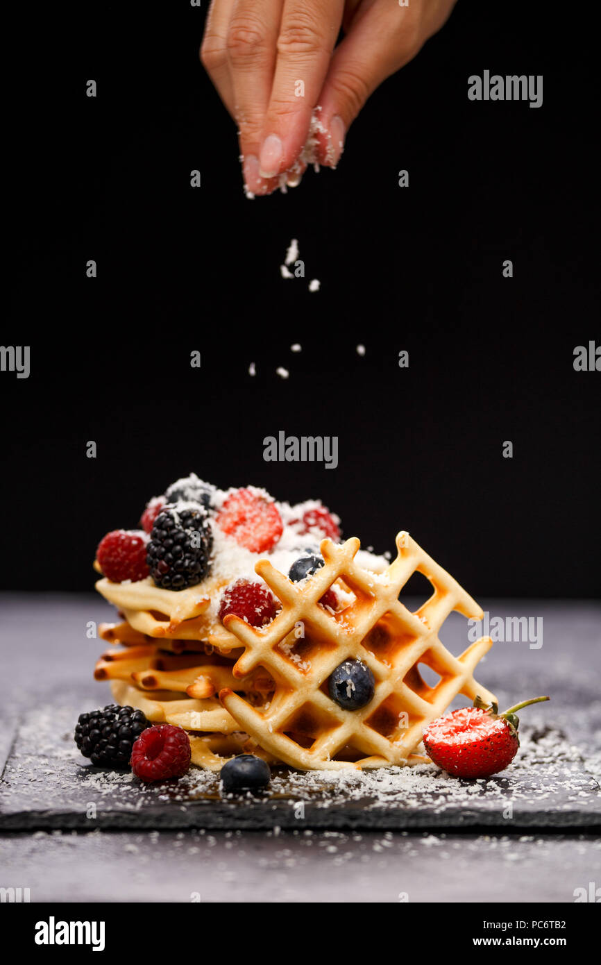 Foto del wafer viennese con lamponi e fragole spolverati con zucchero a velo sulla lavagna contro sfondo bianco Foto Stock
