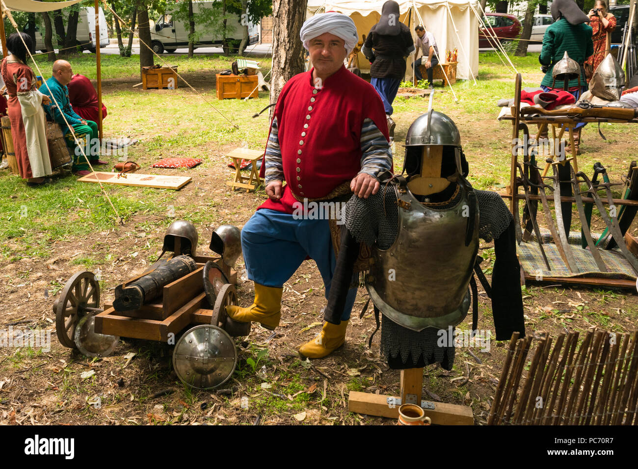 Tulcea, Romania - 14 Luglio 2018: Attore vestito ottoman turk warrior pone circondato da armi medievali, cannone, spade e testa e corpo armor Foto Stock