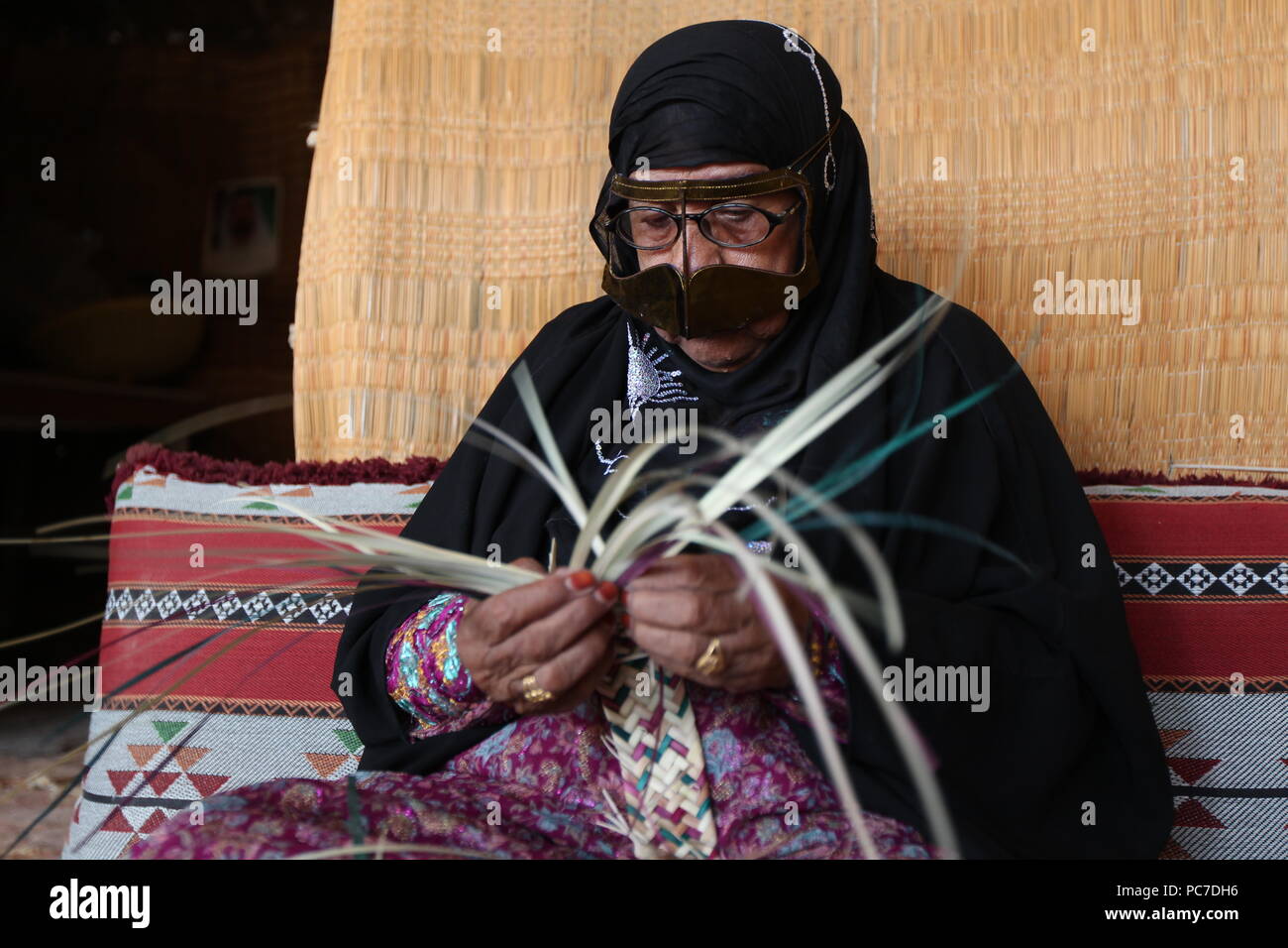 Una donna negli EMIRATI ARABI UNITI, sportive un materiale metallico burqa con henna morì dita, intreccia cesti di paglia e stuoie di foglie di palmo al villaggio del patrimonio culturale in Fujairah. Foto Stock