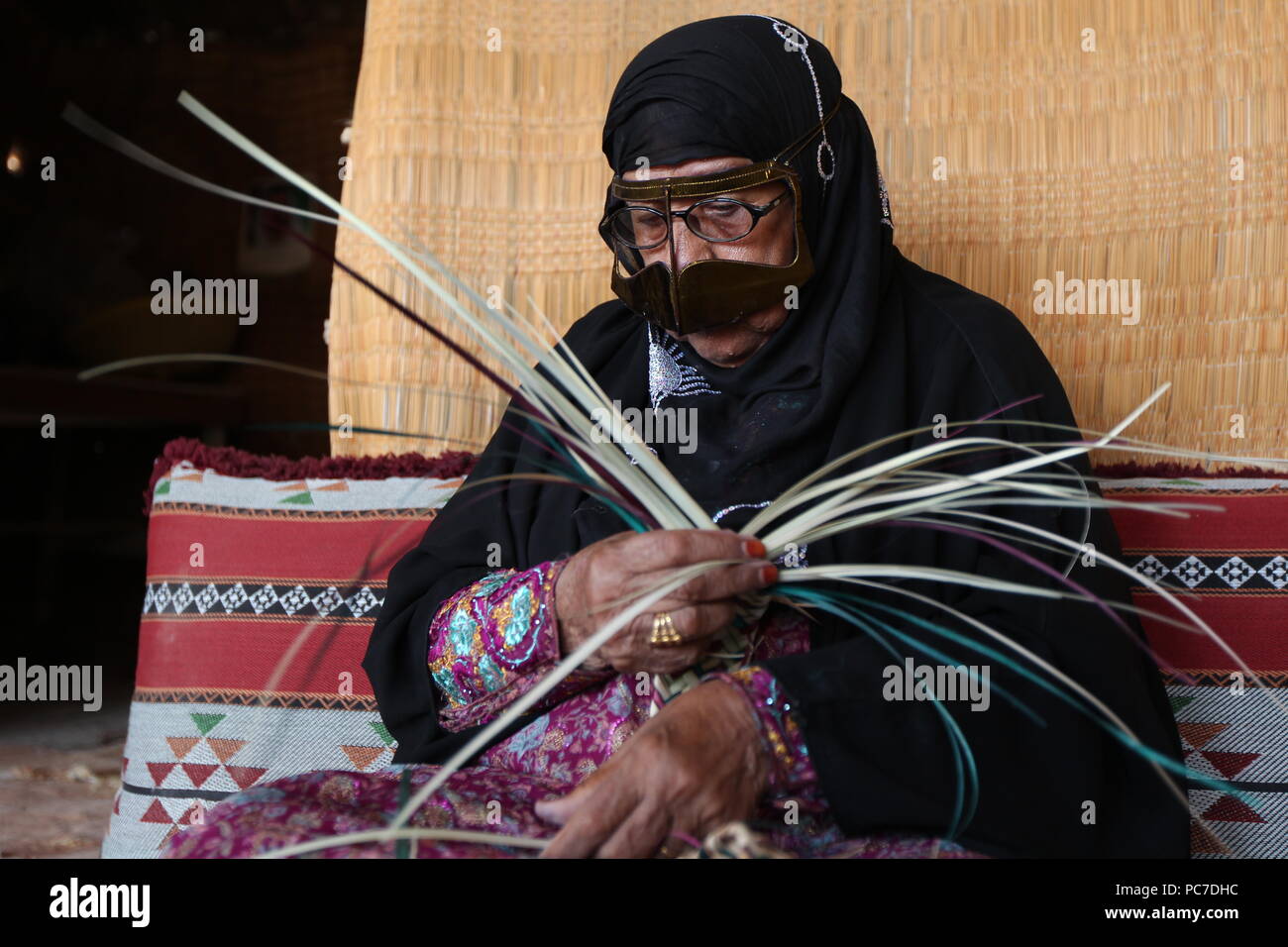 Una donna negli EMIRATI ARABI UNITI, sportive un materiale metallico burqa con henna morì dita, intreccia cesti di paglia e stuoie di foglie di palmo al villaggio del patrimonio culturale in Fujairah. Foto Stock