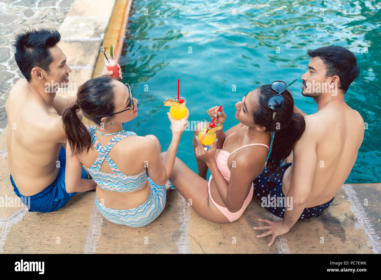 Due giovani coppie di bere un cocktail mentre vi rilassate insieme alla piscina Foto Stock