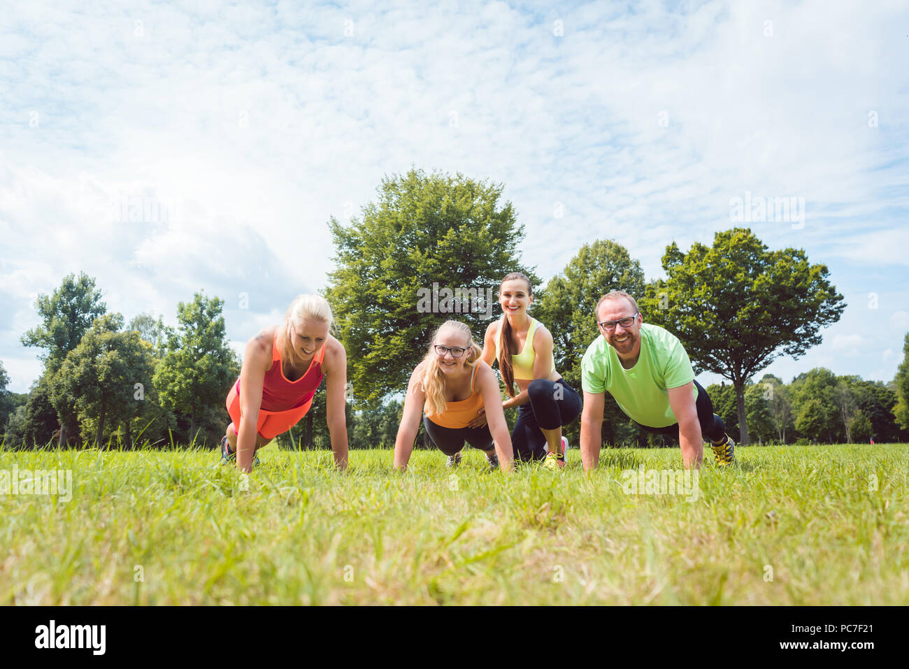 Famiglia facendo push-up in natura sotto la guida di un allenatore di fitness Foto Stock