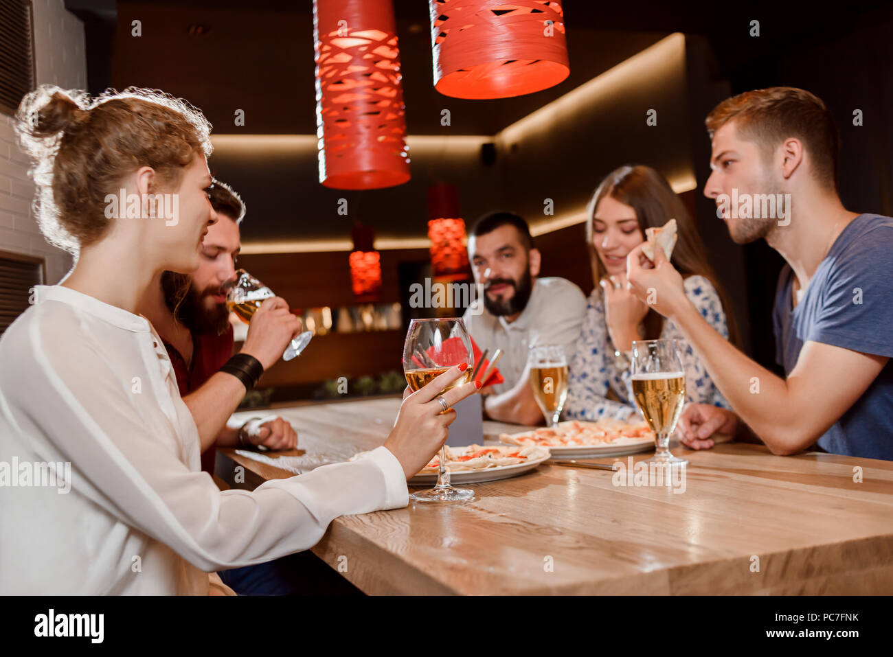 Chiudere gli amici seduti insieme in pizzeria e appendere fuori. Le donne e gli uomini di parlare, di mangiare pizza e bere birra e vino. Concetto di gastronomia, la cucina e il cibo delizioso. Foto Stock