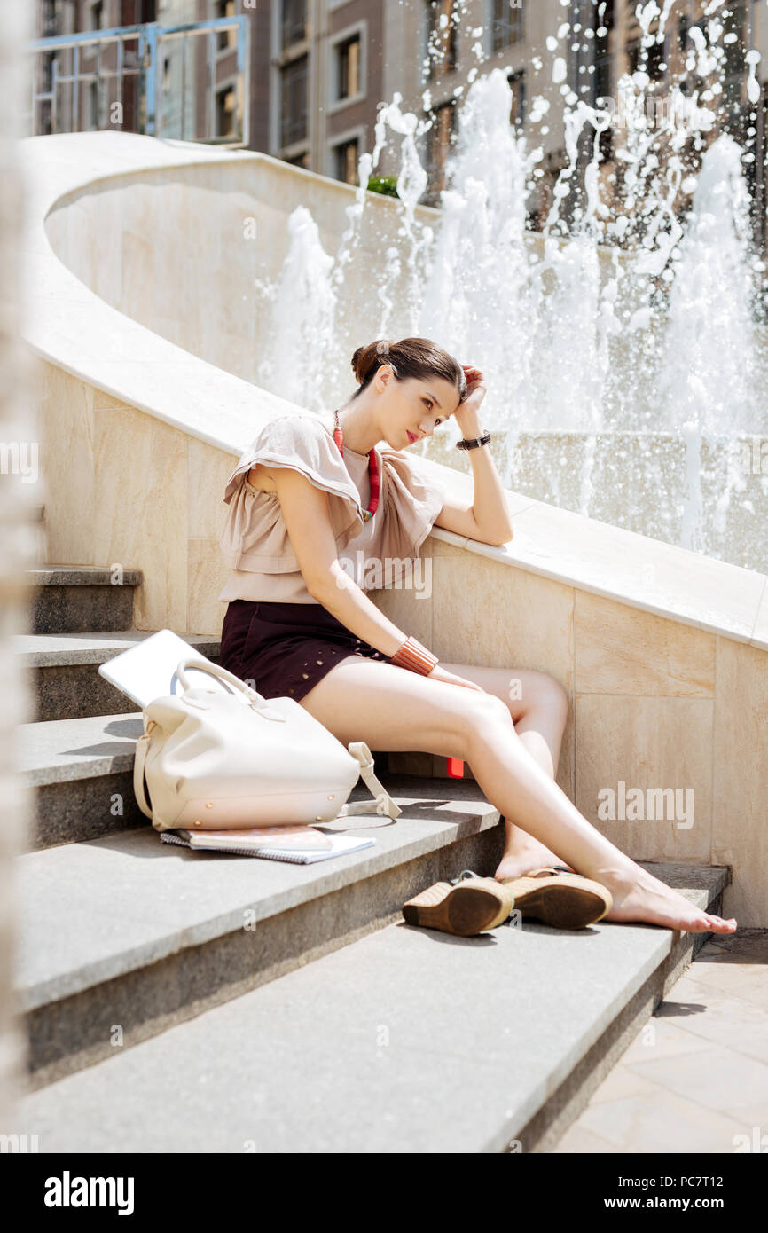 Piacevole giovane donna seduta vicino alla fontana Foto Stock