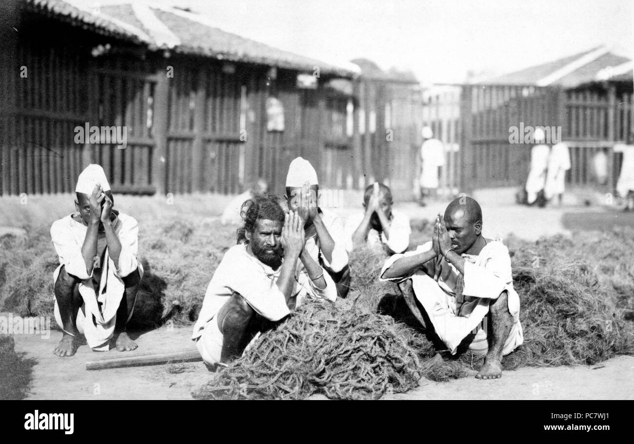 Fotografia mostra cinque detenuti maschi squatting con mani premuti insieme nel mezzo di un materiale fibroso a Rangoon, Birmania 1910-1920 Foto Stock