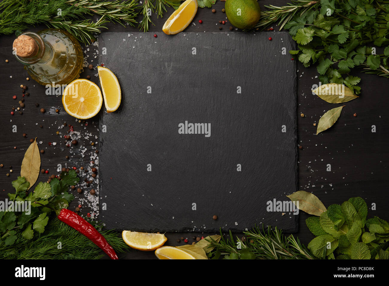 Nero ardesia bordo con erbe fresche e le fette di limone con olio di oliva Foto Stock