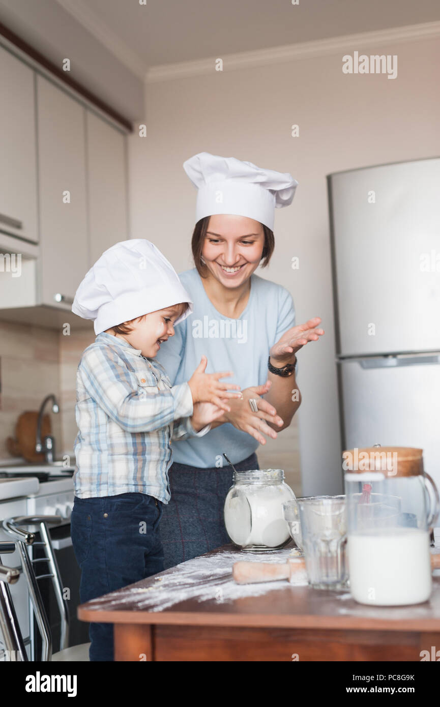 La madre e il bambino battendo le mani durante la preparazione di impasto in cucina Foto Stock