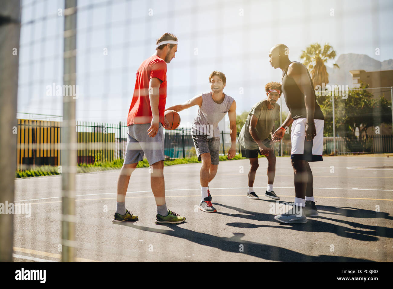 Quattro uomini giocare a basket in un campo di pallacanestro in una giornata di sole. Gli uomini praticano la pallacanestro talento nel dribbling. Foto Stock