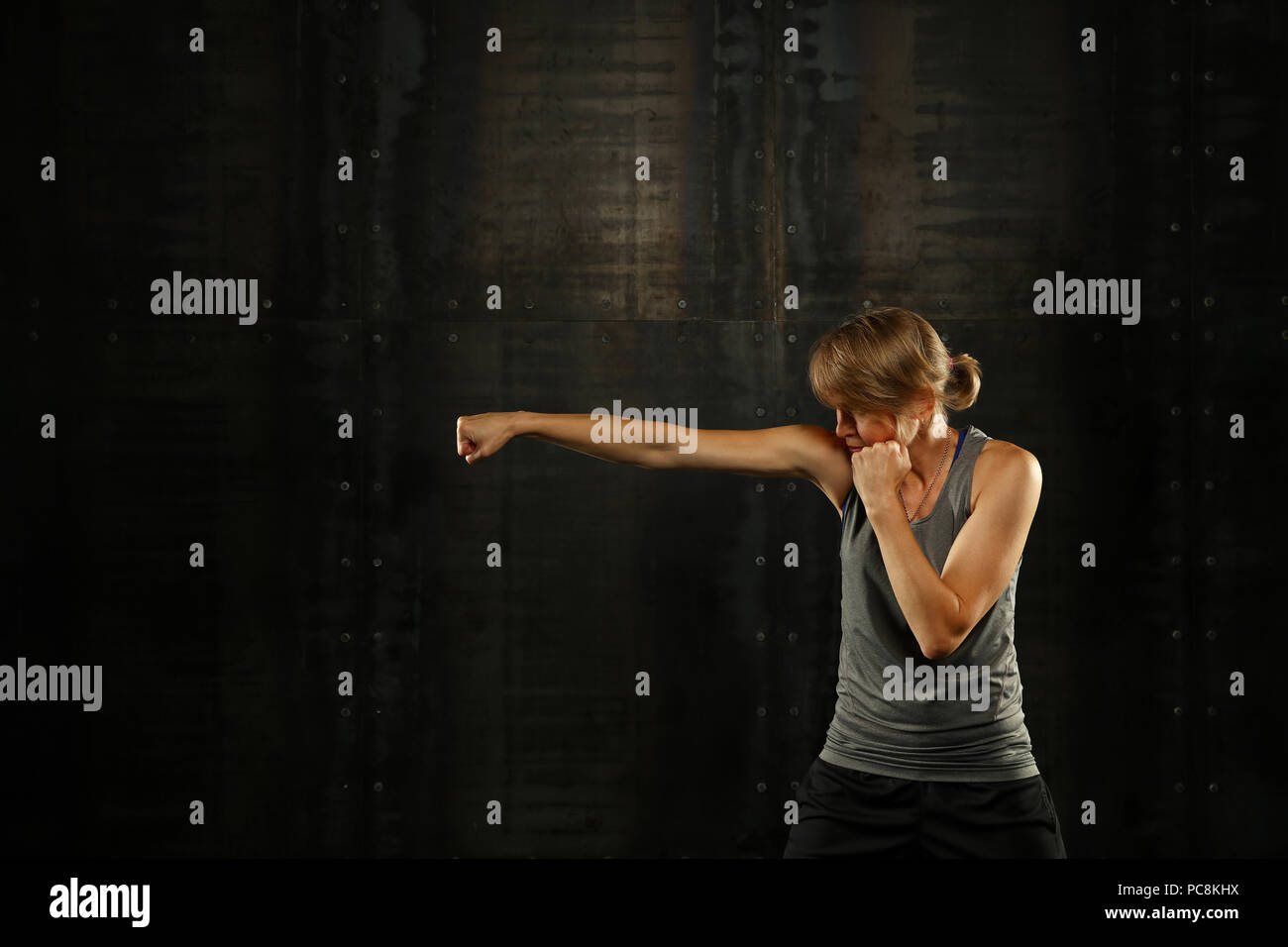 Close up side Visualizza profilo ritratto di una giovane età media athletic donna shadow boxing in abbigliamento sportivo in palestra su sfondo scuro, guardando lontano Foto Stock