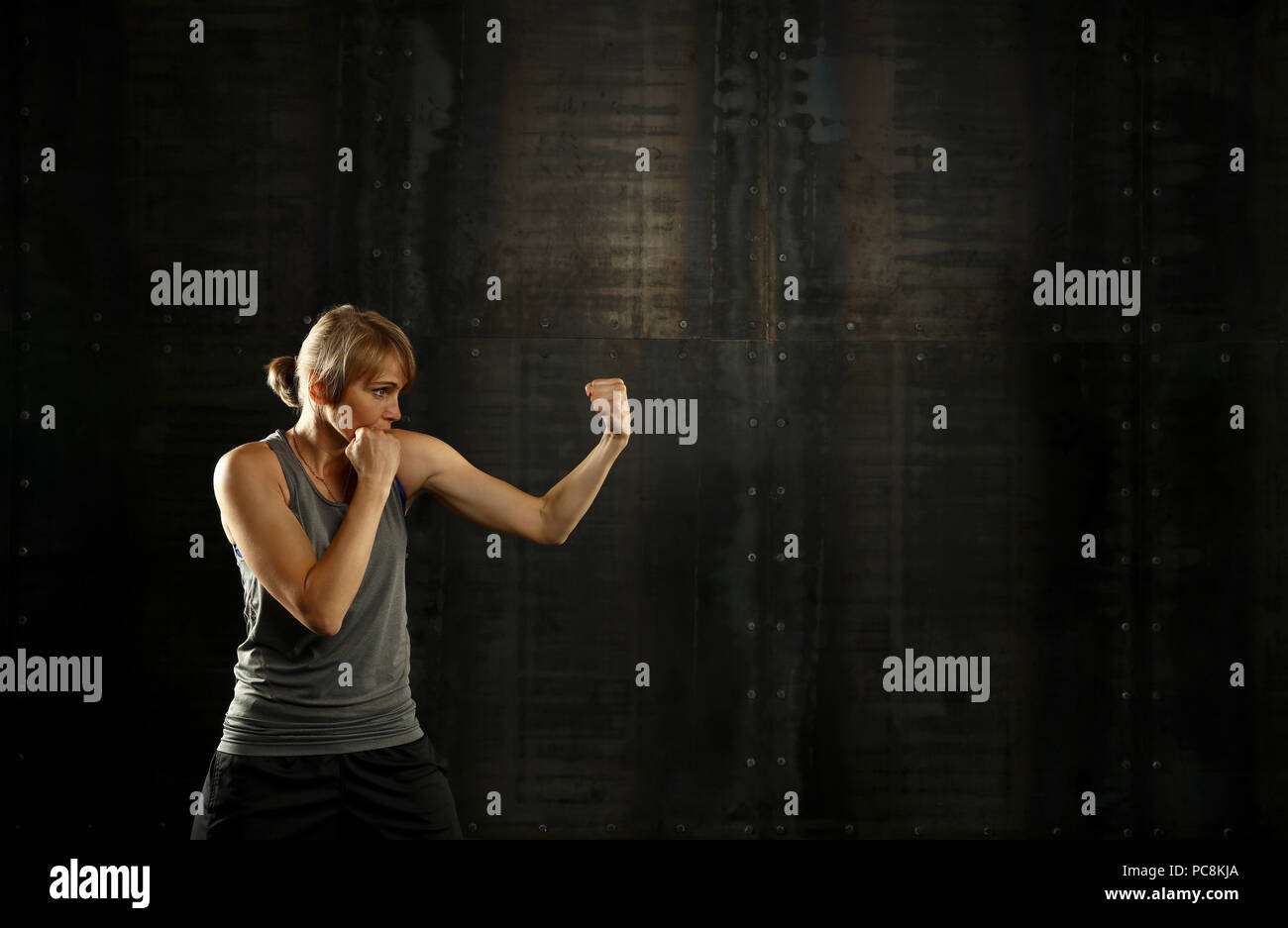 Close up side Visualizza profilo ritratto di una giovane età media athletic donna shadow boxing in abbigliamento sportivo in palestra su sfondo scuro, guardando lontano Foto Stock